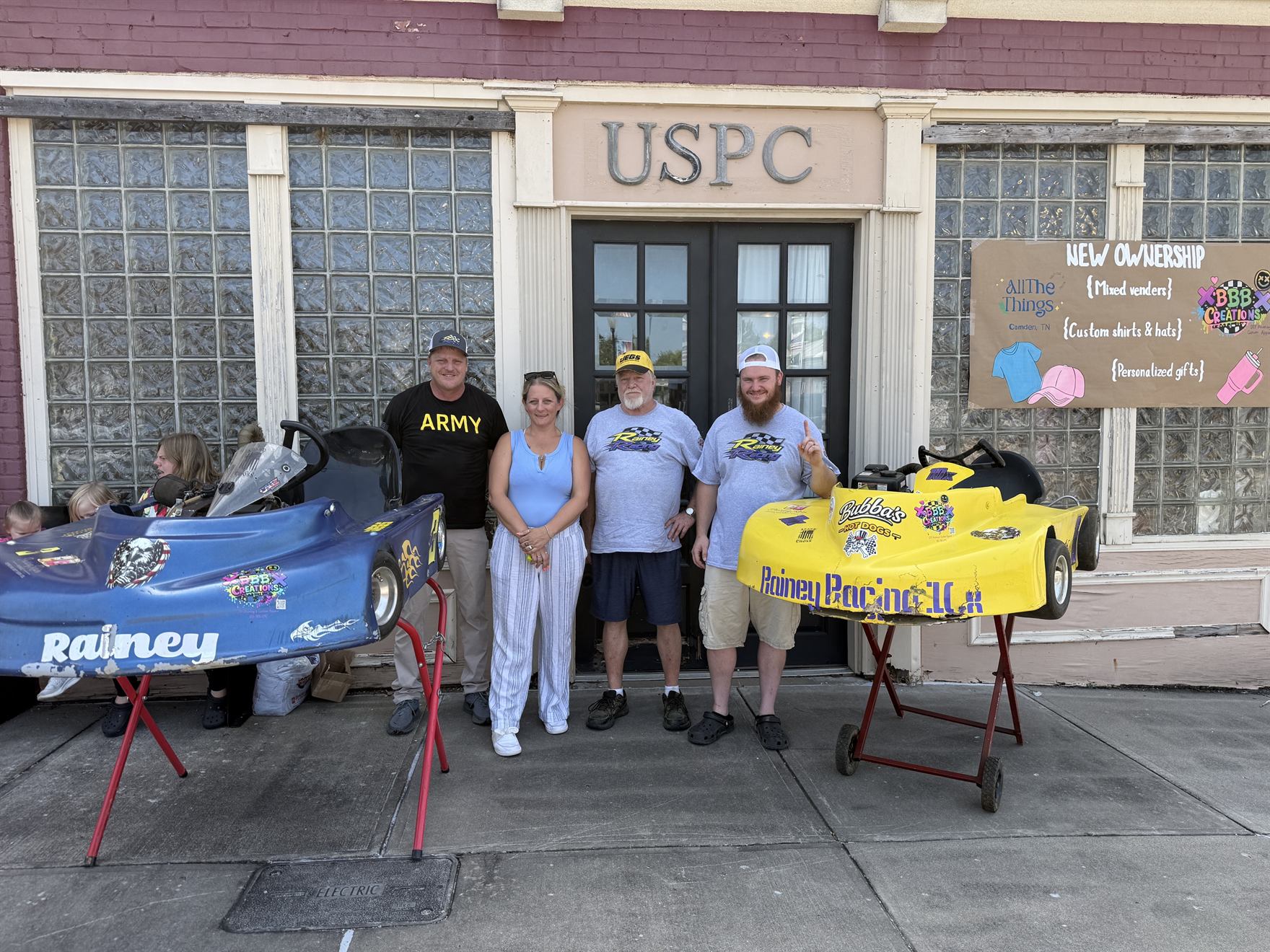 Ronnie Rainey, Brandi Bath, Ronnie Rainey Sr. and Travis Rainey with both karts outside the shop on the Camden Court Square