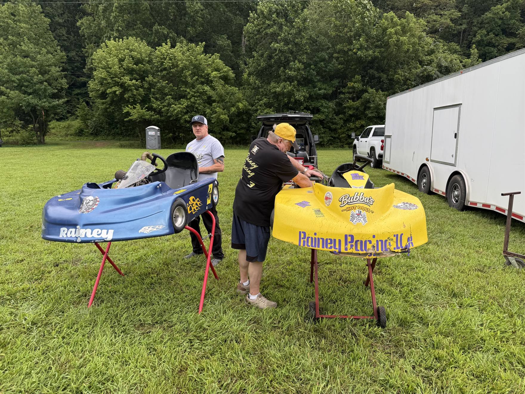Travis's yellow 10X and Ronnie's blue 3 karts up on stands in the grass pits at Sleepy Hollow Speedway