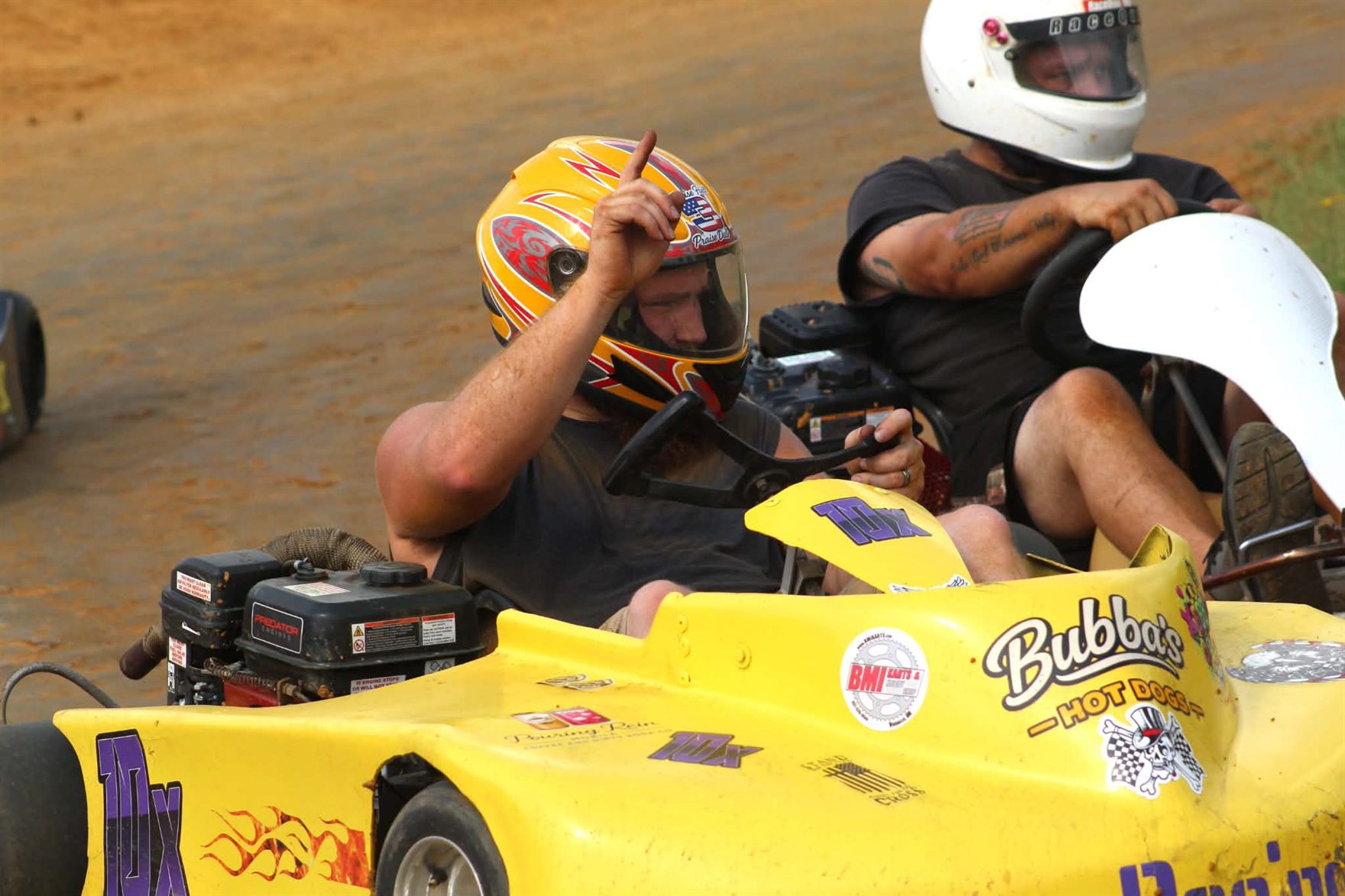 Travis pointing a finger to the sky from the seat of the 10X alongside another kart