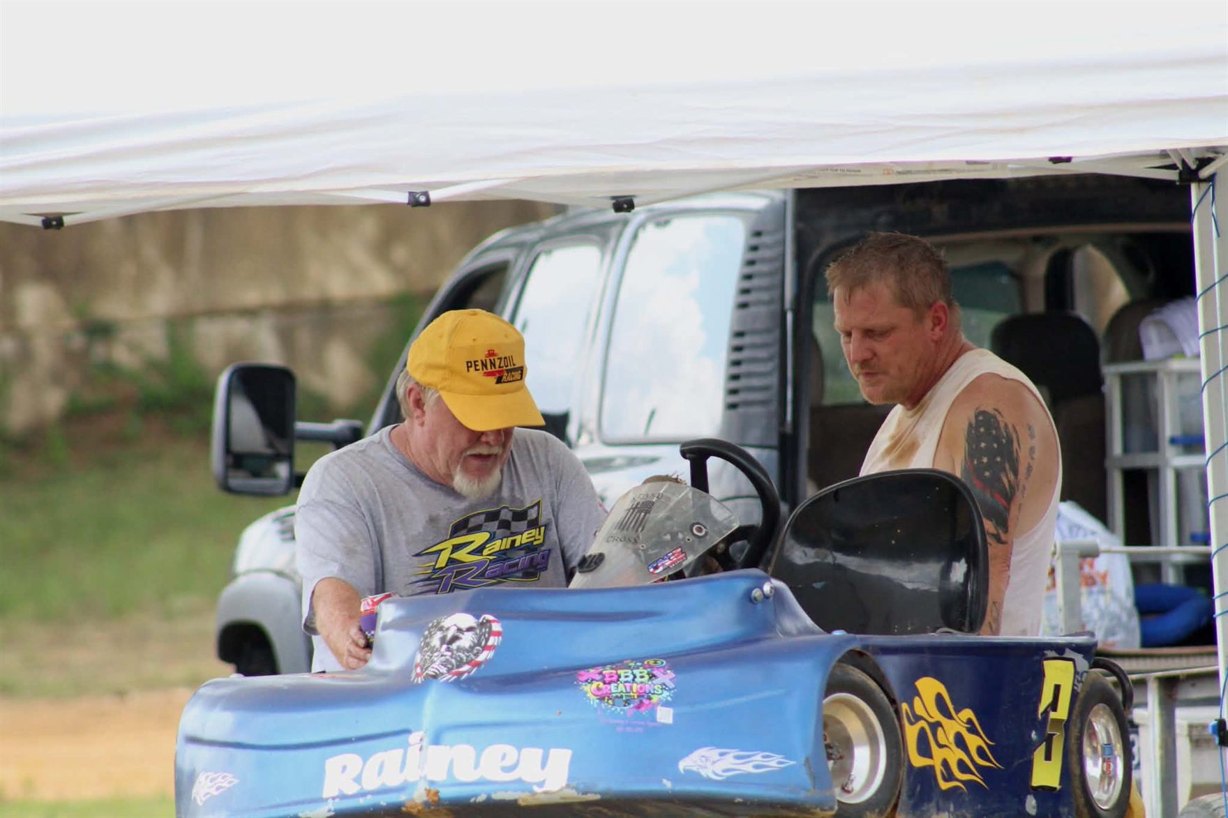 Ronnie Rainey Sr. and Ronnie Rainey working on the blue 3 kart under the pit canopy